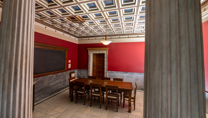 The Greek Room, with ancient Greek columns surrounding the room, and a wooden table with inscriptions in Greek in the center